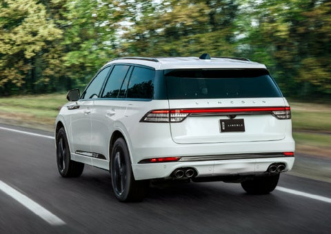 A white 2026 Lincoln Aviator® SUV is being driven away down a road lined with colorful trees. | Dave Sinclair Lincoln in Ballwin MO