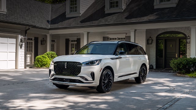 A white 2026 Lincoln Aviator® SUV is parked in the driveway of a luxury home. | Dave Sinclair Lincoln in Ballwin MO