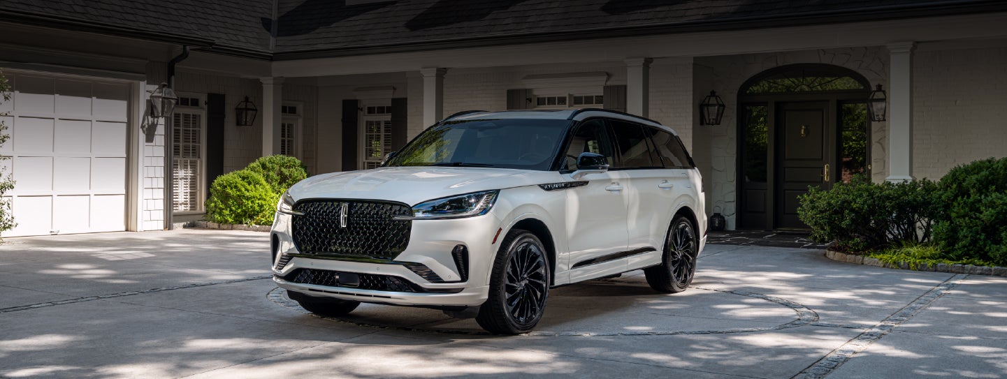 A white 2026 Lincoln Aviator® SUV is parked in the driveway of a luxury home. | Dave Sinclair Lincoln in Ballwin MO
