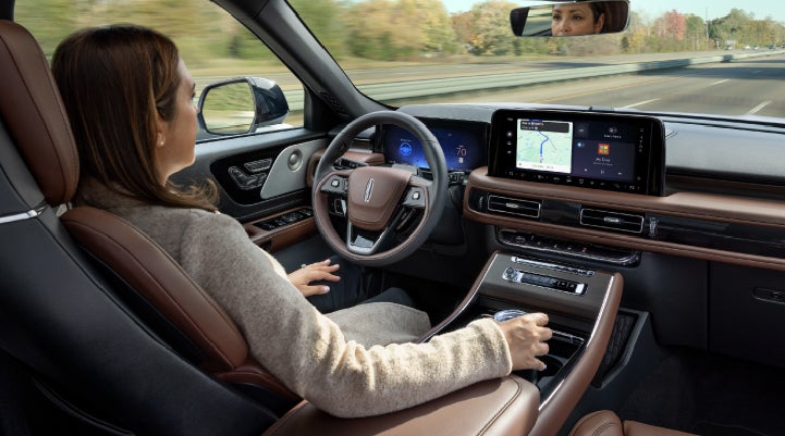 A 2027 Lincoln Aviator® SUV is being driven hands-free on a highway lined with trees. | Dave Sinclair Lincoln in Ballwin MO