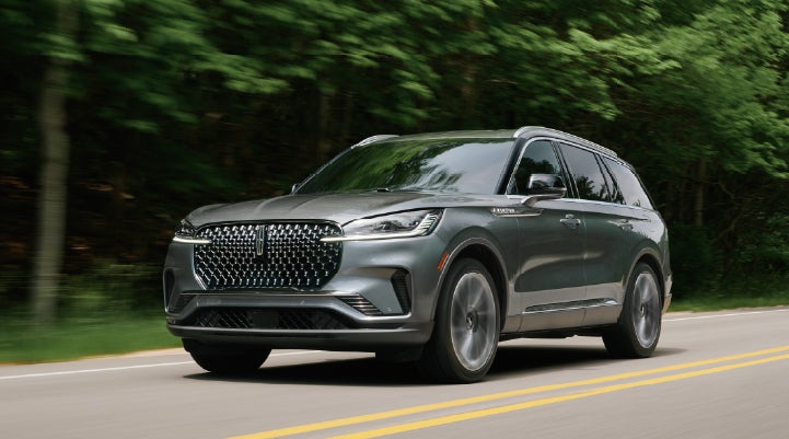 A 2027 Lincoln Aviator® SUV is being driven down a road lined with trees. | Dave Sinclair Lincoln in Ballwin MO