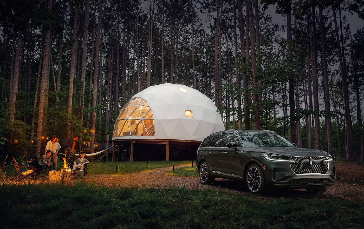 Lincoln Aviator parked beside a lit dome tent in a pine forest at dusk