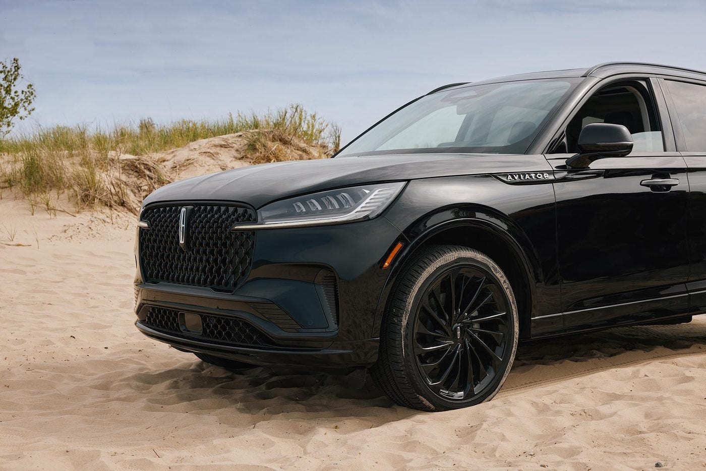 Black Lincoln Aviator parked on a sandy beach with dune grass