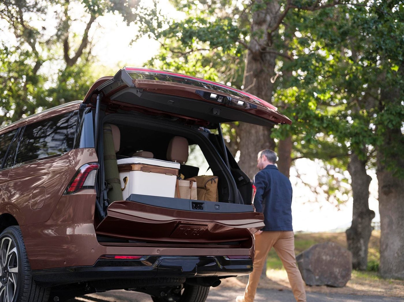 Maroon Lincoln Navigator with the liftgate open and a man carrying a bag nearby under trees